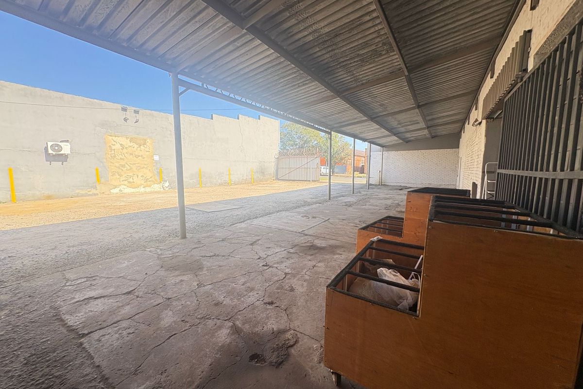 Covered industrial outdoor workspace featuring a concrete floor, metal roof structure, and perimeter walling, suitable for storage or loading operations.