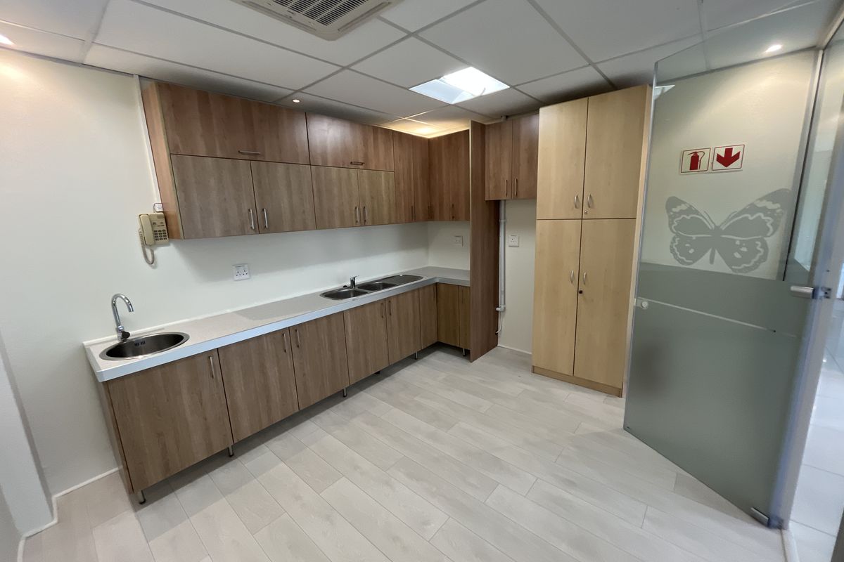 A clean office kitchenette featuring wood-finish cabinetry, dual stainless steel sinks, laminate countertops, and a suspended ceiling with integrated air conditioning.