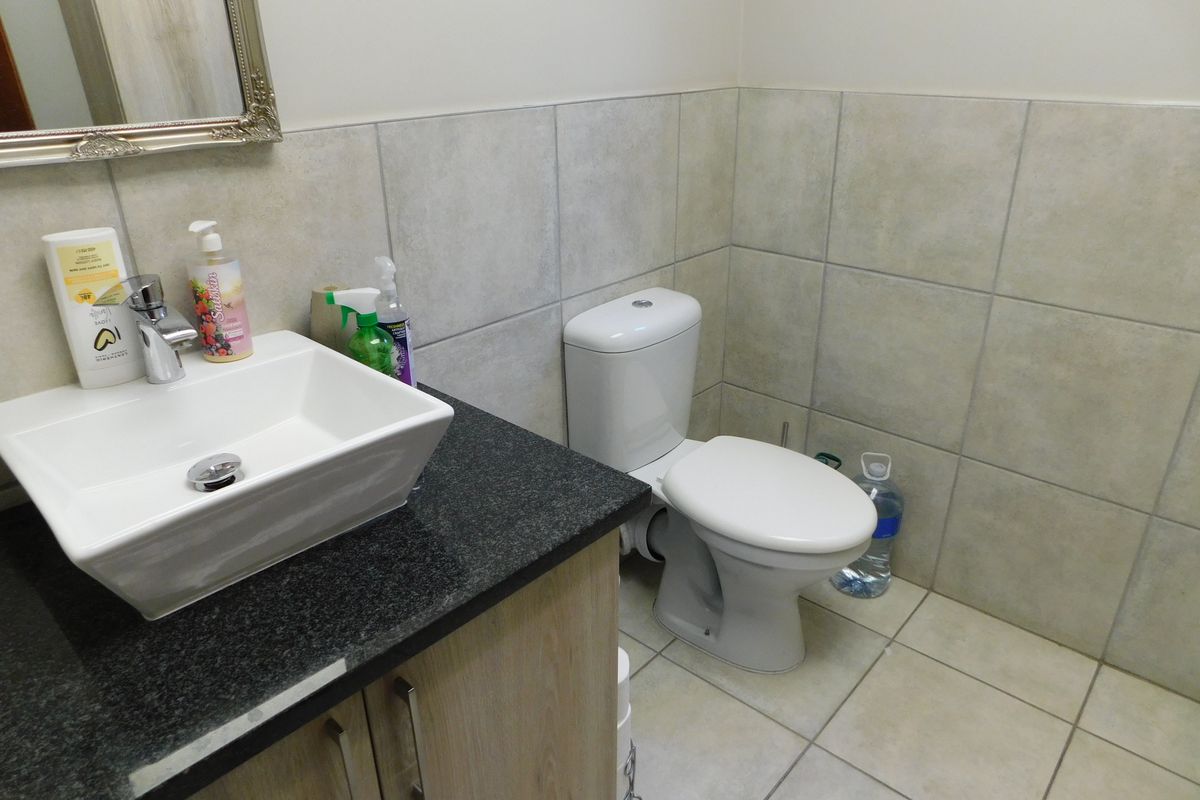 A functional office bathroom featuring a modern vessel sink, granite countertop, vanity cabinet, and a standard white toilet with tiled walls and flooring.