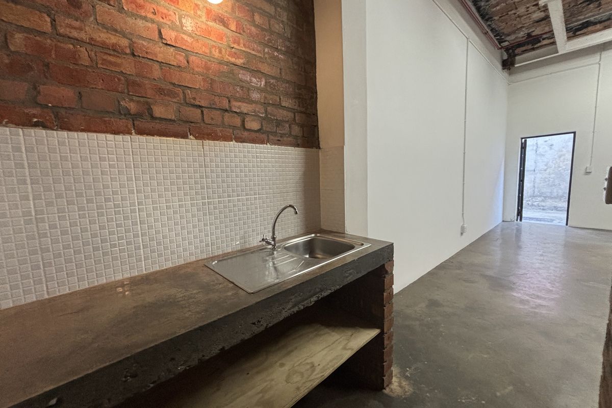 Industrial-style kitchenette area featuring a concrete countertop, stainless steel sink, and exposed brick wall finish within an open-plan workspace.