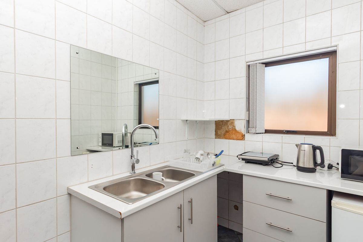 A functional office kitchenette featuring a double stainless steel sink, tiled walls, and built-in cabinetry with a laminate countertop.