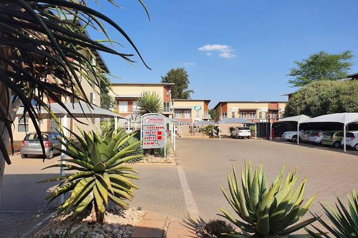 Exterior view of an office park complex featuring paved parking bays with shade cloth carports and established garden landscaping.