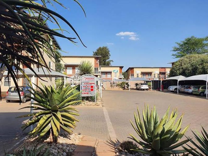 Exterior view of an office park complex featuring paved parking bays with shade cloth carports and established garden landscaping.