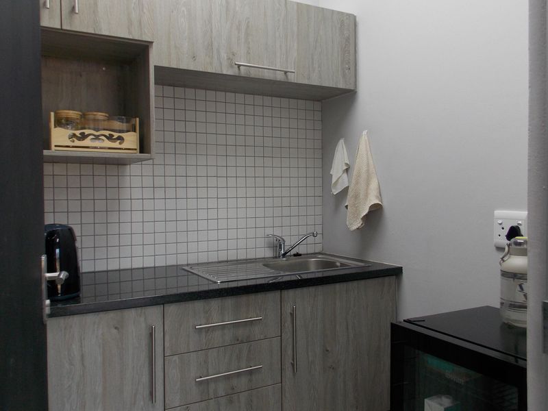 A compact office kitchenette featuring wood-look laminate cabinetry, a stainless steel sink, and a clean tiled backsplash.
