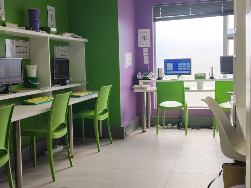 A functional office space featuring built-in desk workstations, integrated shelving, tiled flooring, and a suspended ceiling with recessed lighting.