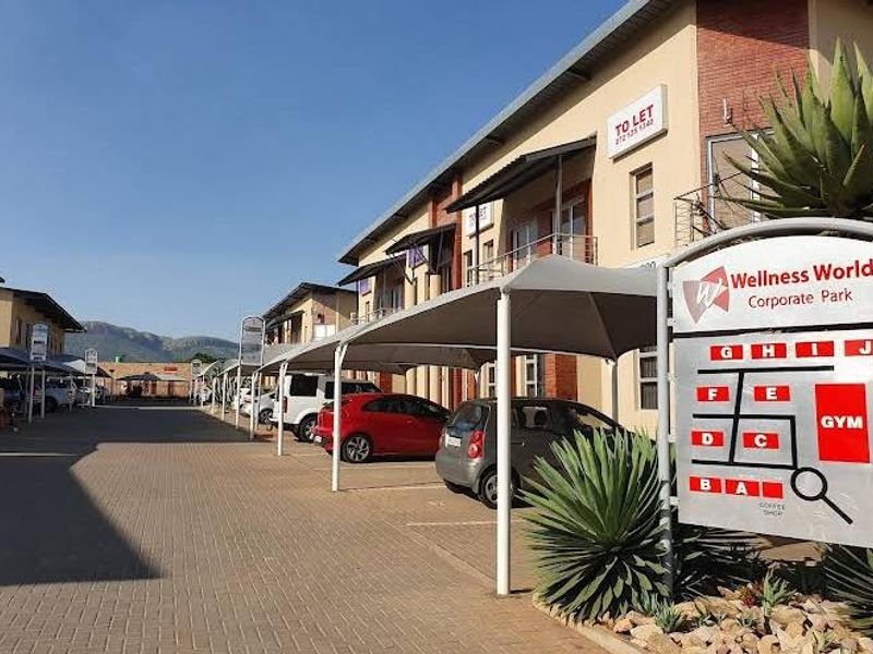 Exterior view of the Wellness World Corporate Park featuring paved parking areas, covered bays, and clear site signage.