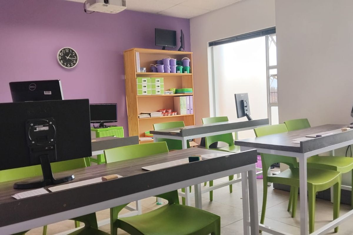 A functional office space featuring large windows for natural light, tiled flooring, and a ceiling-mounted projector, suitable for a collaborative work or training environment.