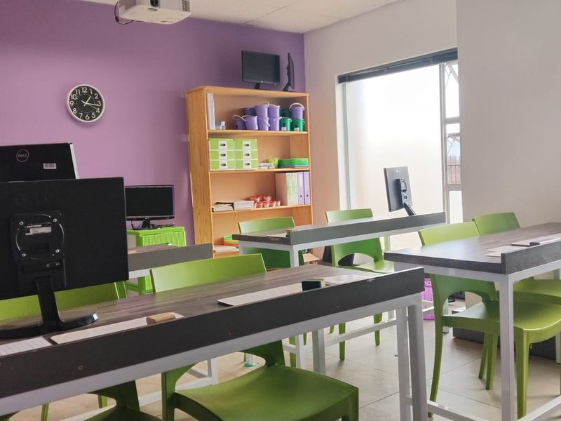 A functional office space featuring large windows for natural light, tiled flooring, and a ceiling-mounted projector, suitable for a collaborative work or training environment.