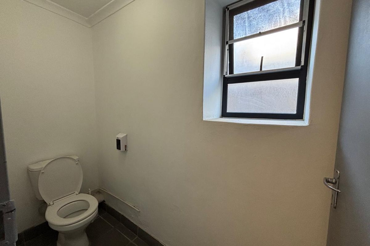 A functional industrial restroom featuring a standard toilet, tiled flooring, and a frosted glass window for natural light and privacy.