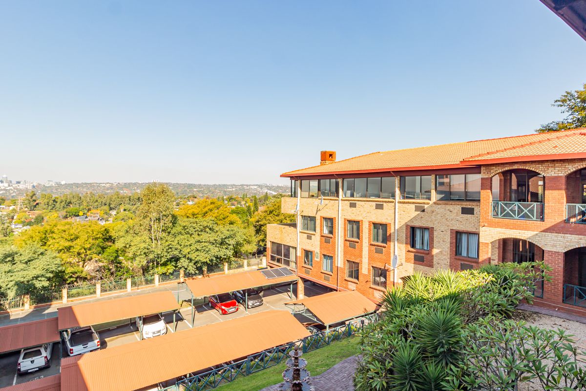 Elevated view of the office complex exterior, featuring brick facade, tiled roofing, and covered parking bays with a scenic urban backdrop.