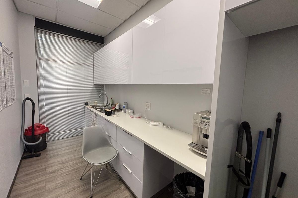 A compact office kitchenette featuring modern white cabinetry, a stainless steel sink, and durable laminate flooring.