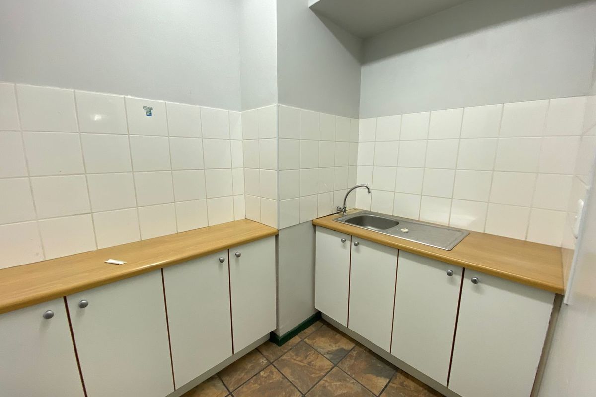 A functional kitchenette area featuring white cabinetry, wood-look laminate countertops, a stainless steel sink, and tiled splashbacks.