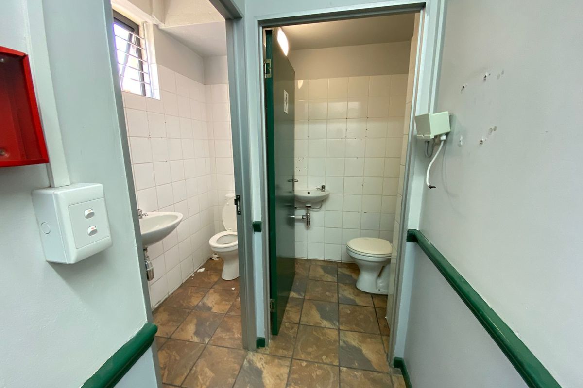 A commercial restroom facility featuring two separate toilet cubicles with wall-mounted basins, tiled flooring, and basic sanitary infrastructure.