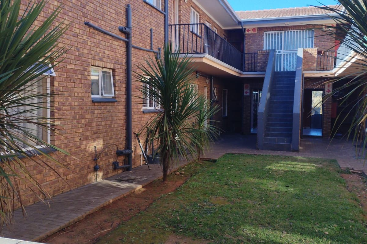 Exterior view of the apartment complex featuring brick facade, external staircase, and a shared courtyard area with lawn.