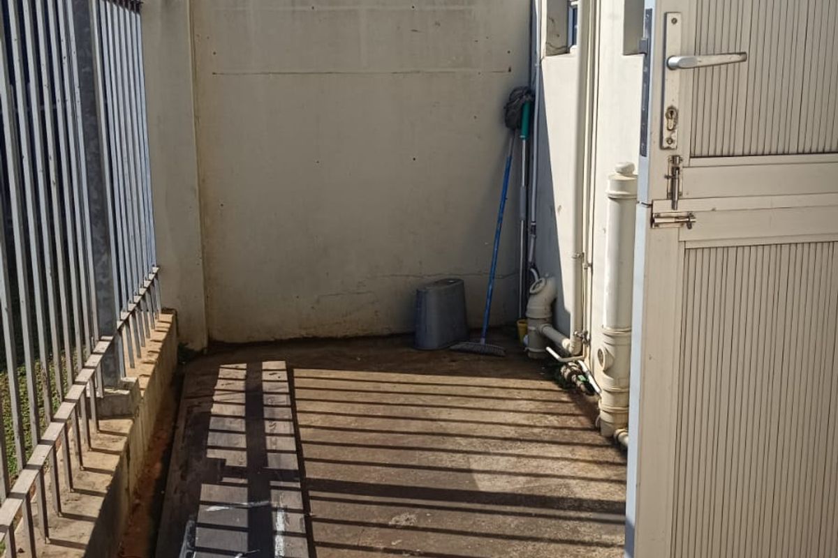A narrow exterior utility area featuring concrete flooring, a perimeter metal fence, and access to the building's rear service entrance.