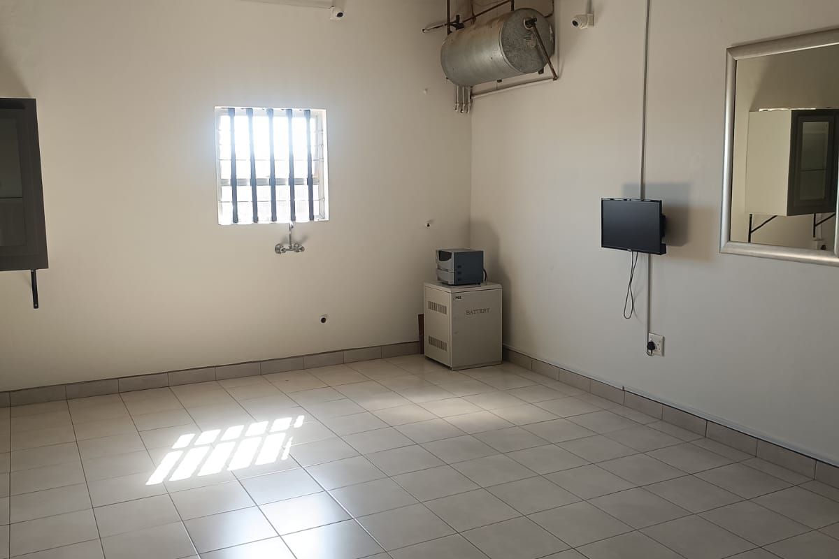 A functional, open-plan commercial utility space featuring tiled flooring, a security-barred window, and exposed ceiling structure.