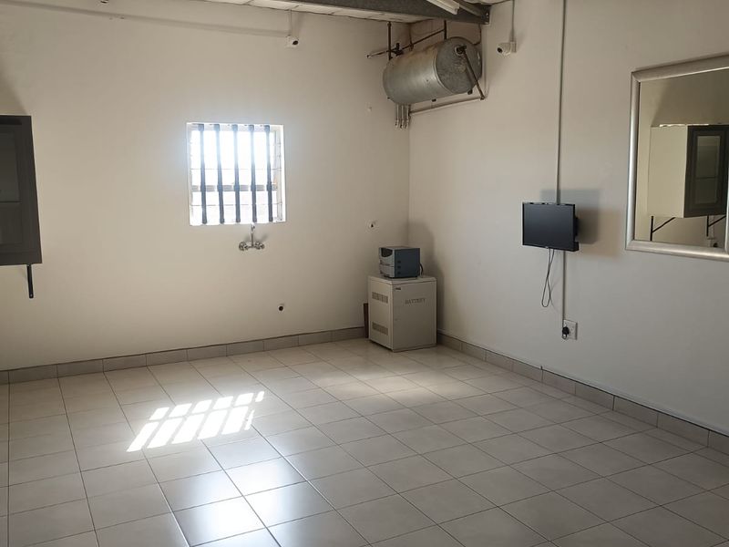 A functional, open-plan commercial utility space featuring tiled flooring, a security-barred window, and exposed ceiling structure.