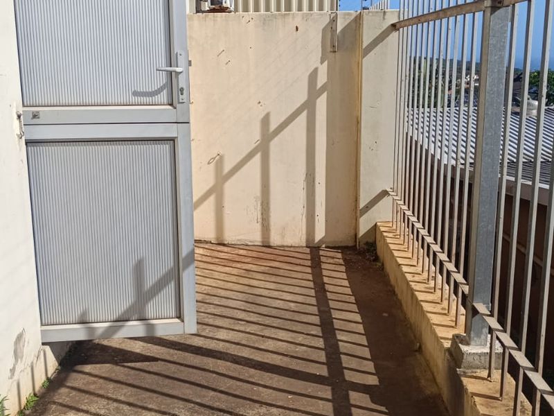An exterior utility area featuring a metal door, concrete flooring, and perimeter security fencing with an electric fence installation.