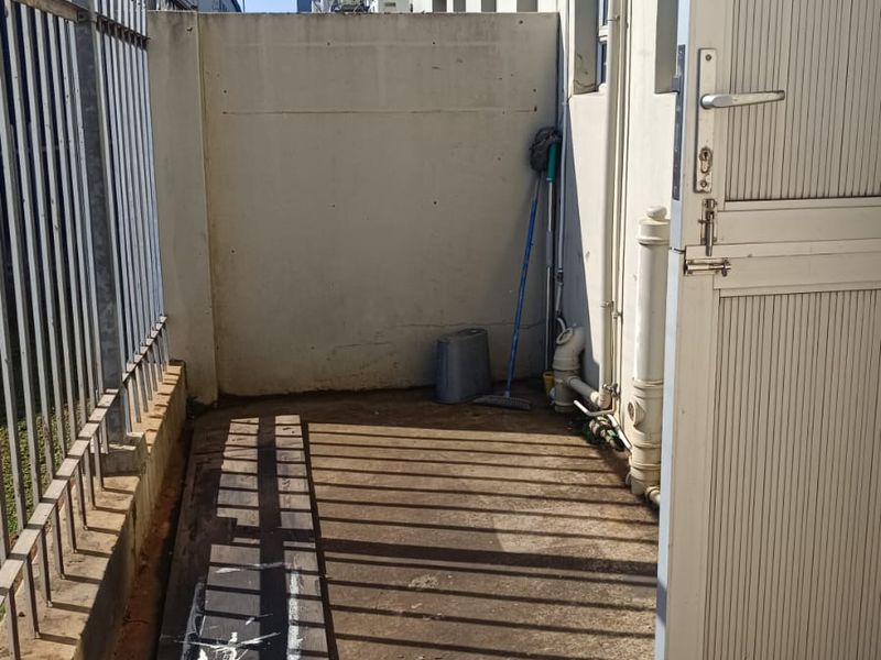 A narrow exterior utility area featuring concrete flooring, a perimeter metal fence, and access to the building's rear service entrance.