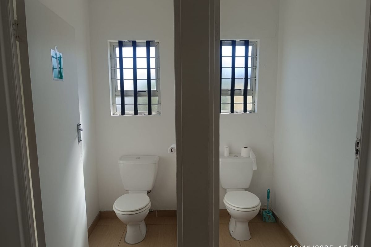 Two separate restroom cubicles featuring white ceramic toilets, tiled flooring, and security bars on the windows.