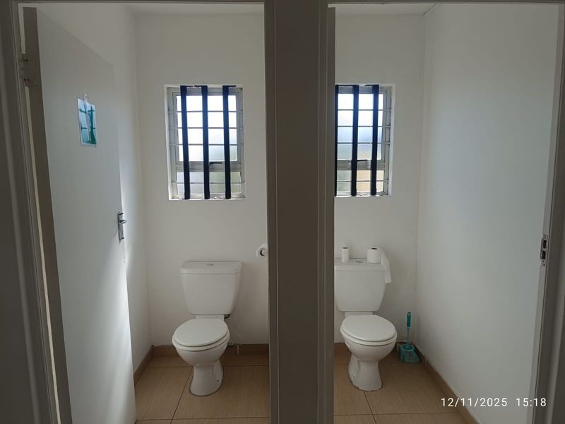 Two separate restroom cubicles featuring white ceramic toilets, tiled flooring, and security bars on the windows.