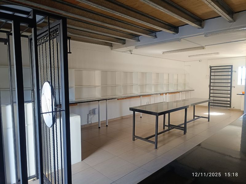 Commercial utility space featuring tiled flooring, built-in wall shelving, and exposed ceiling structure, suitable for storage or workshop use.