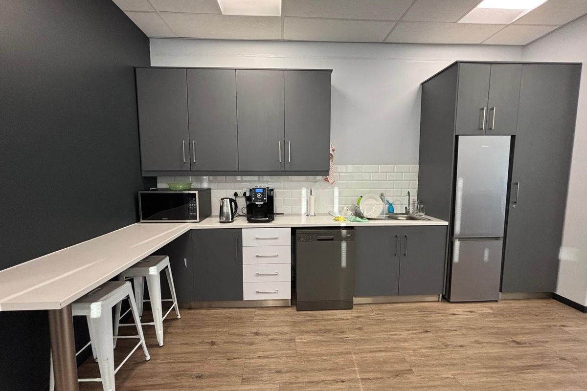 Modern office kitchenette featuring dark grey cabinetry, white subway tile backsplash, integrated dishwasher, and a built-in breakfast bar area.