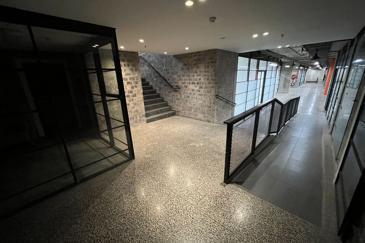 Modern commercial hallway featuring exposed brickwork, terrazzo flooring, a metal staircase, and a ramp with industrial-style mesh railing.