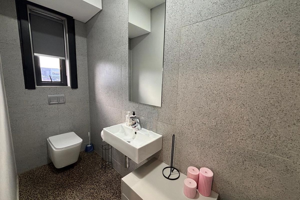 Modern office bathroom featuring grey terrazzo-style wall tiling, a wall-mounted basin, and a sleek wall-hung toilet.