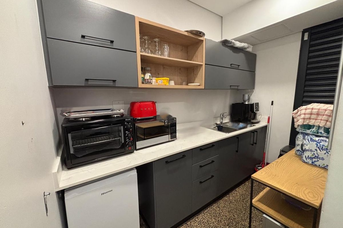 Compact kitchenette featuring modern grey cabinetry, light wood open shelving, stone-look countertops, and a stainless steel sink.