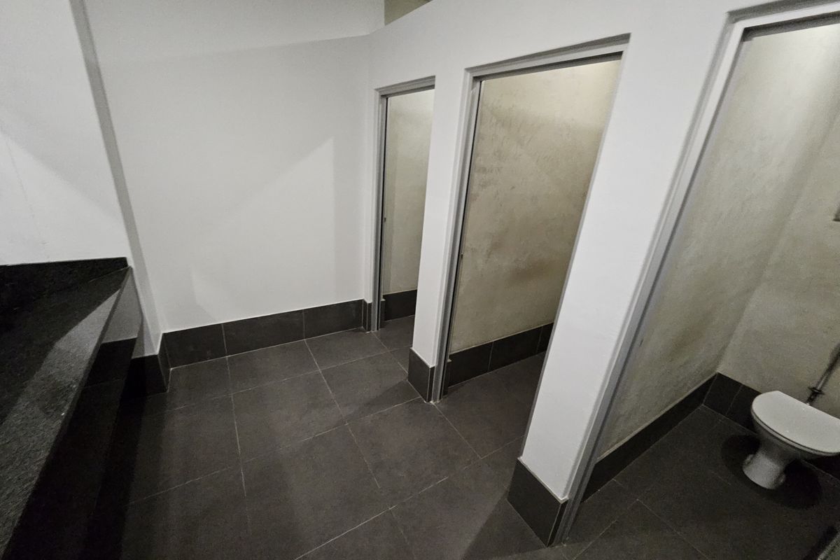 A functional office restroom featuring dark floor tiling, a granite vanity counter, and multiple individual toilet cubicles.