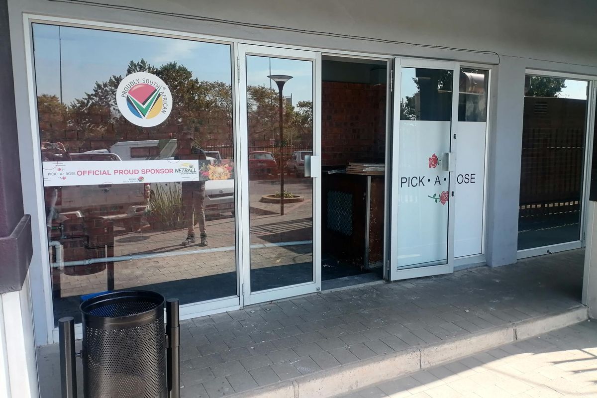 Commercial storefront entrance featuring large glass sliding doors, brickwork accents, and paved walkway access.