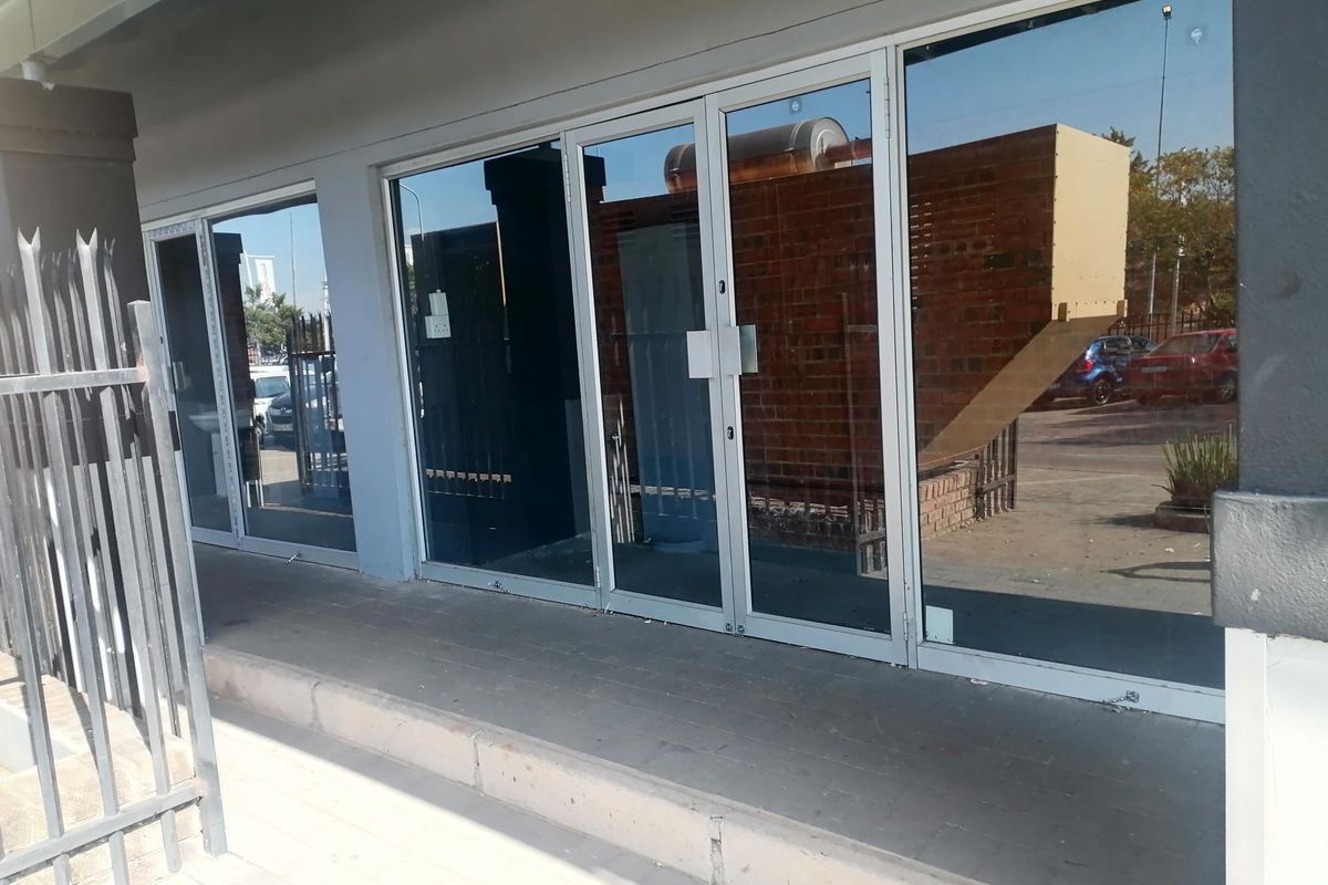 Commercial storefront entrance featuring large glass panel doors and windows with a paved walkway and metal security fencing.
