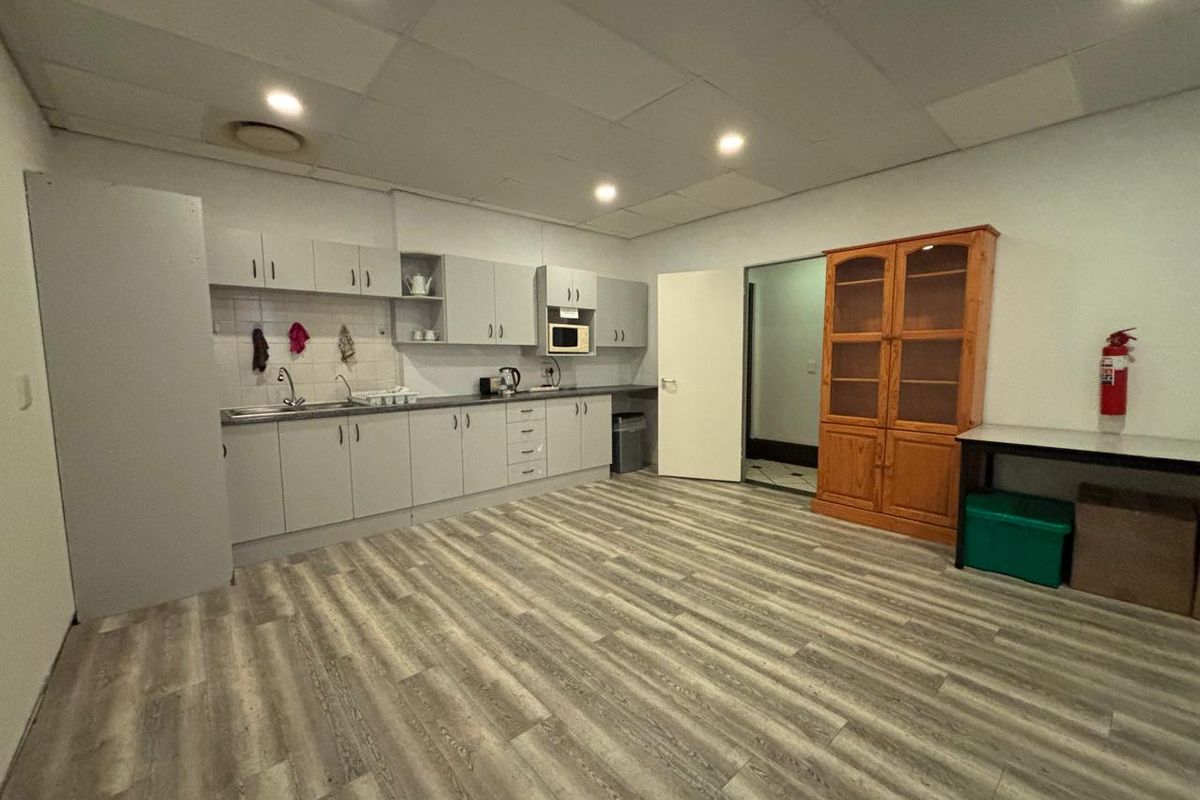 A functional office kitchenette featuring grey cabinetry, a stainless steel sink, recessed ceiling lighting, and wood-look vinyl flooring.
