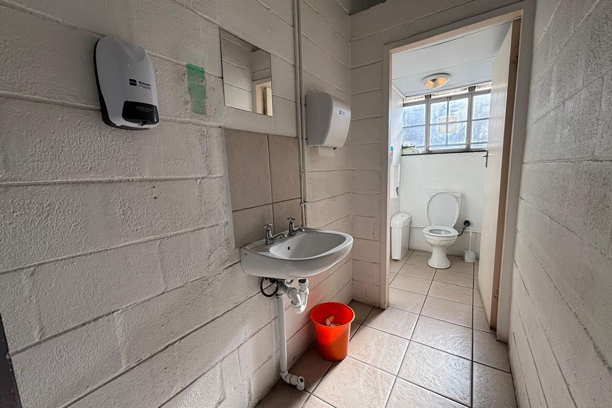 A functional industrial-style restroom featuring a wall-mounted basin, tiled flooring, and a separate toilet cubicle with natural light.