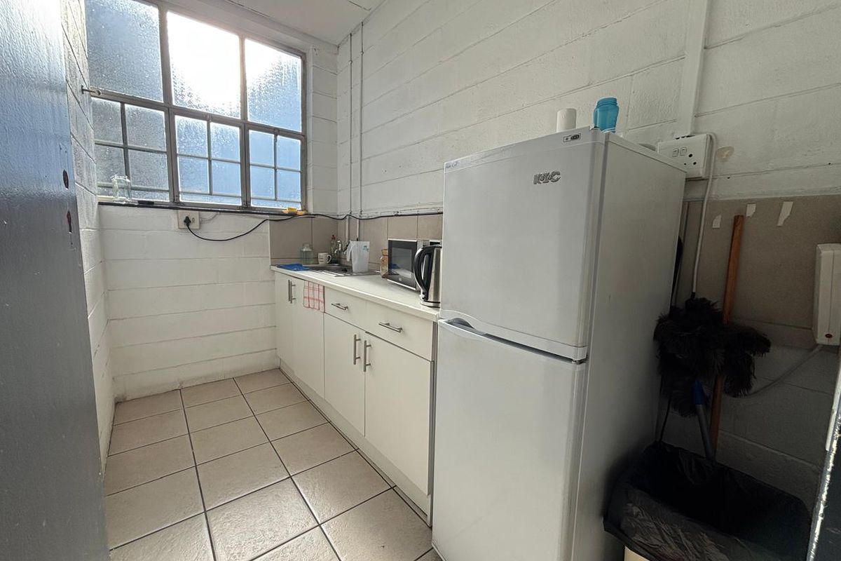 A functional industrial-style kitchenette featuring white cabinetry, tiled flooring, and a large window providing natural light.