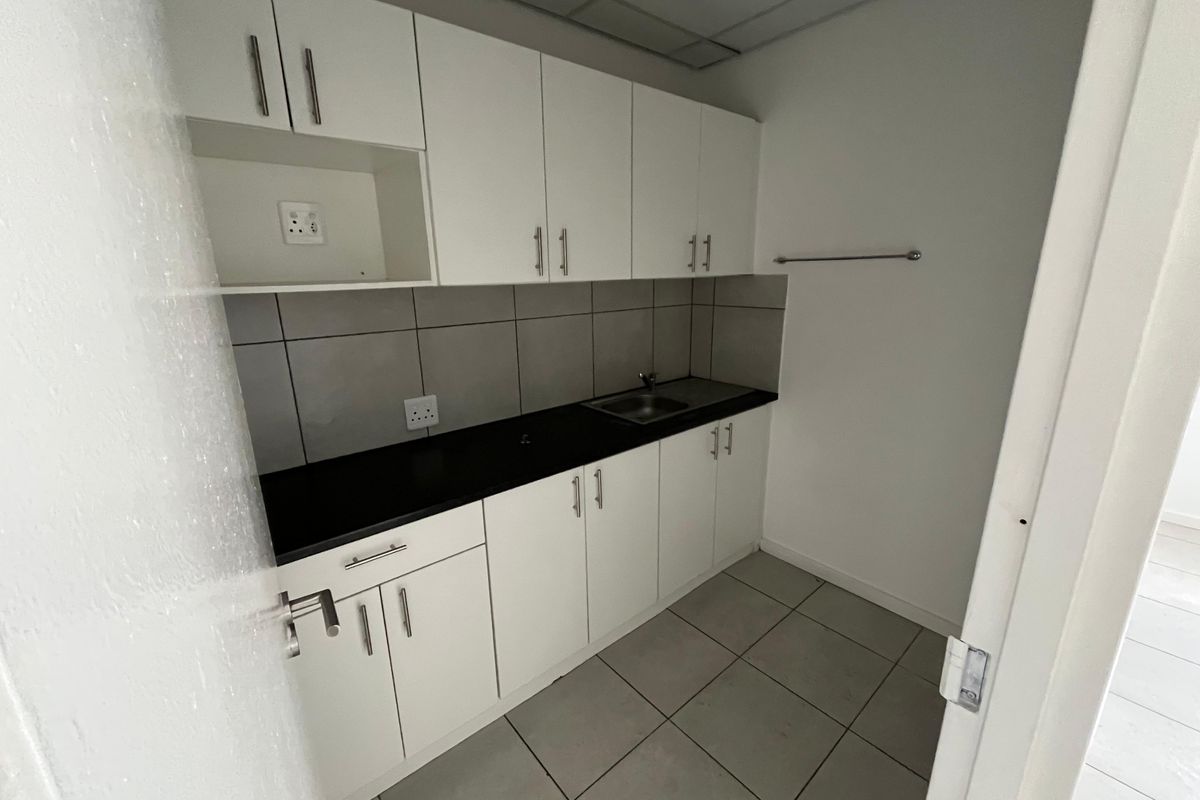 A compact kitchenette featuring white cabinetry, a dark countertop, a stainless steel sink, and grey tiled backsplash.