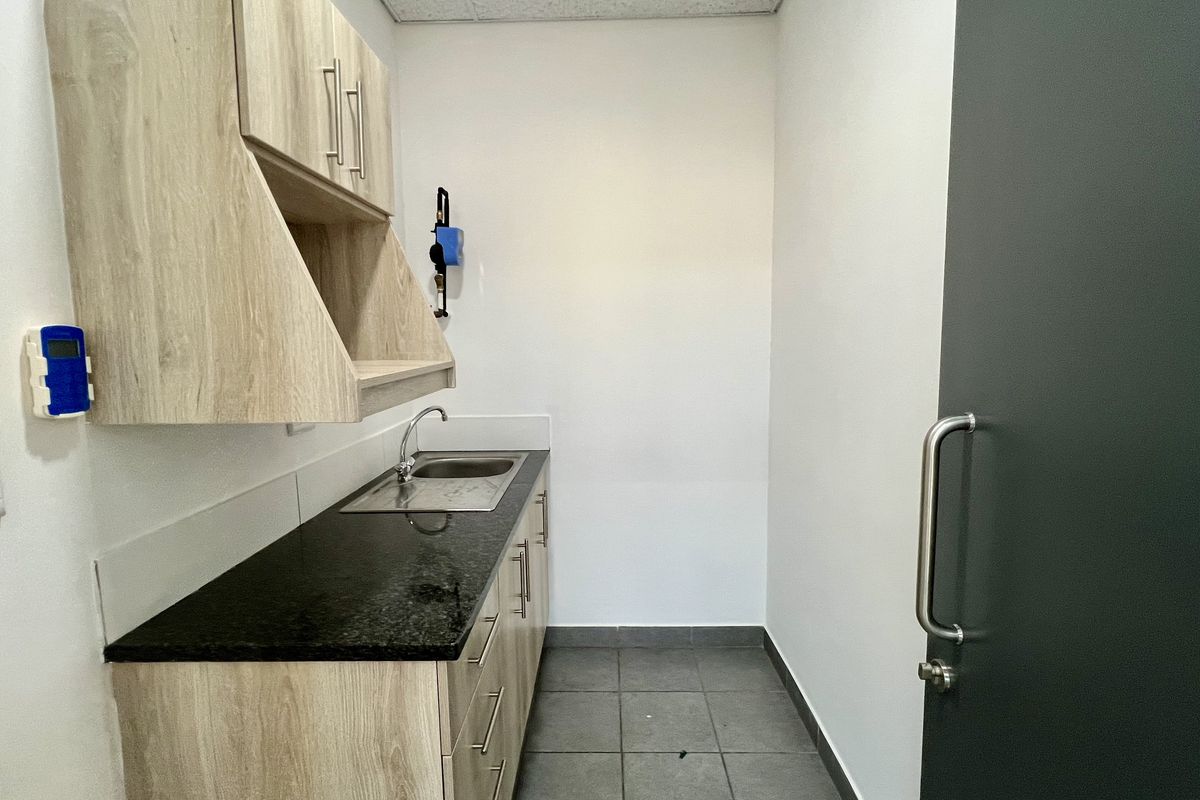 A compact office kitchenette featuring light wood-grain cabinetry, a dark granite countertop, a stainless steel sink, and tiled flooring.