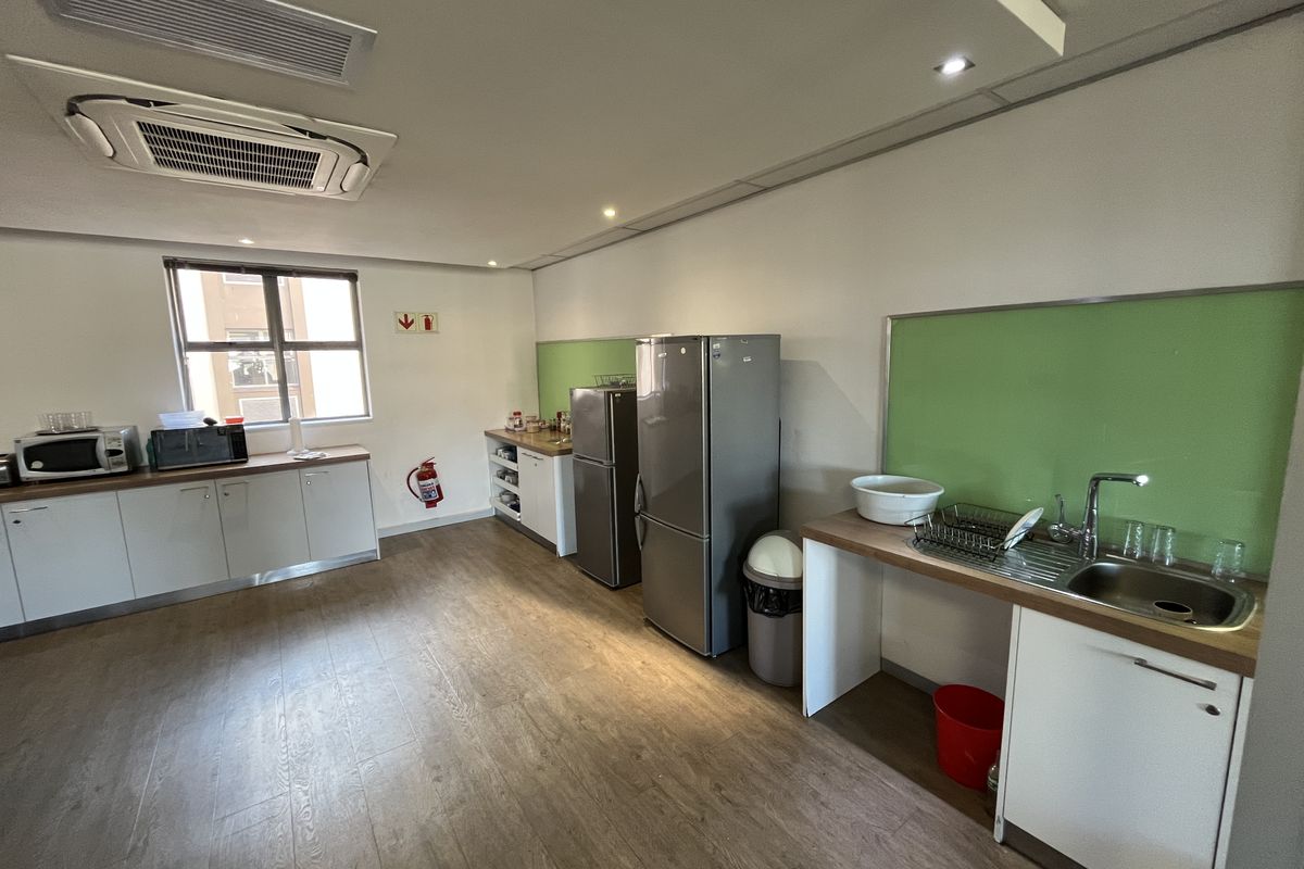 A functional office kitchenette featuring white cabinetry, wood-look flooring, a stainless steel sink, and integrated ceiling air conditioning.