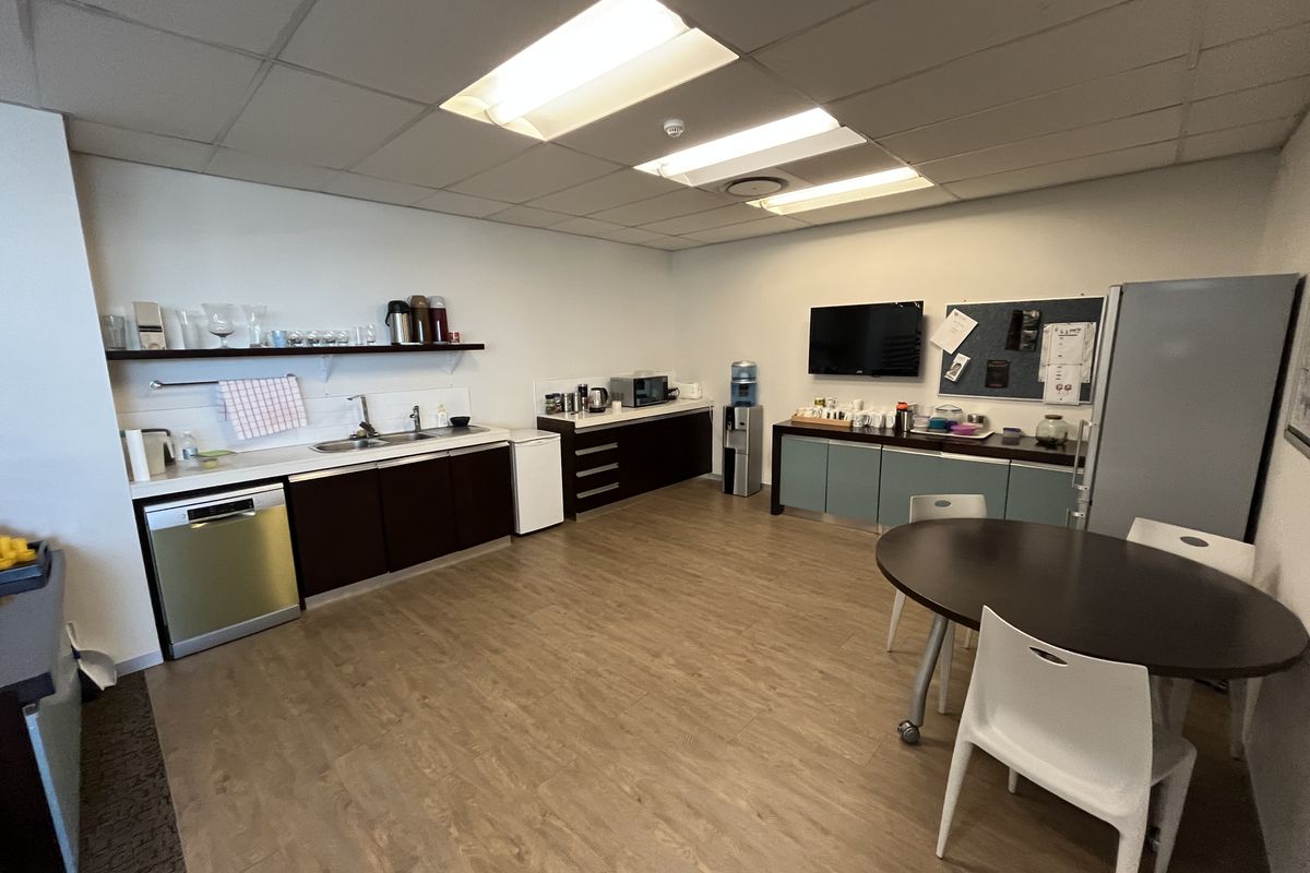 A functional office kitchenette featuring laminate flooring, built-in cabinetry, a stainless steel sink, and an integrated dishwasher.
