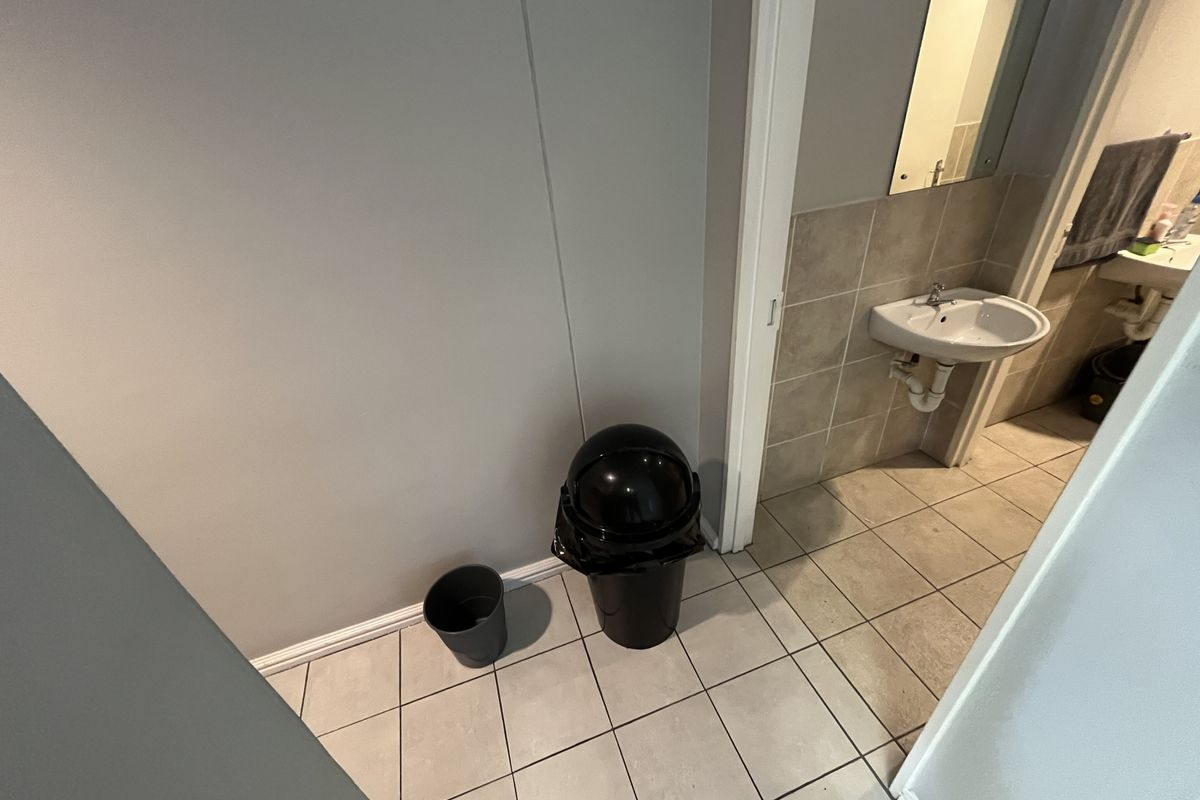 A functional office bathroom featuring tiled flooring, a wall-mounted basin, and a mirror.
