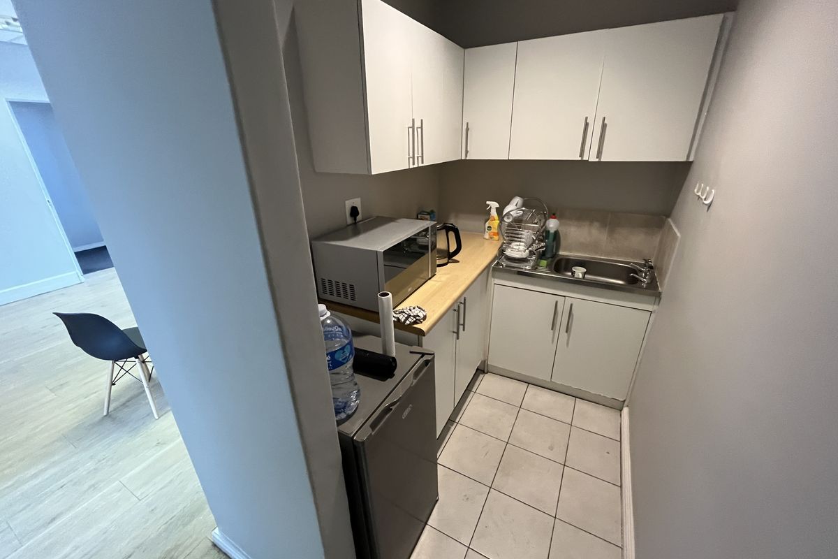Compact office kitchenette featuring white cabinetry, a stainless steel sink, and tiled flooring, providing essential utility space for a professional environment.