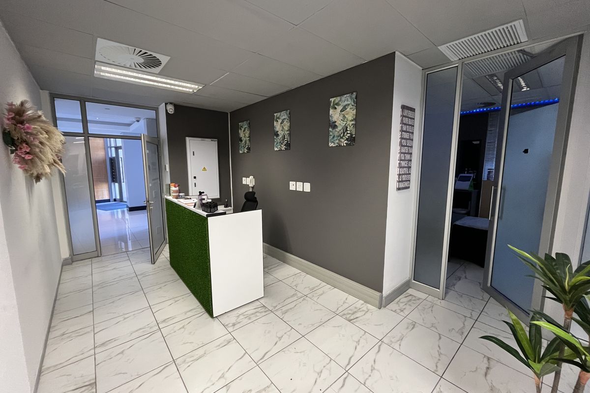 A modern office reception area featuring marble-look tiled flooring, a built-in reception desk, and glass partition doors leading to adjacent office spaces.