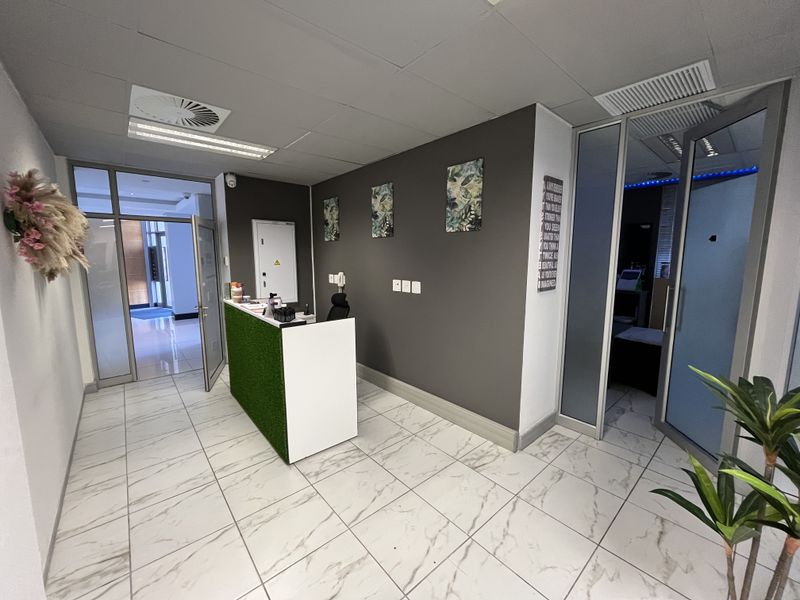 A modern office reception area featuring marble-look tiled flooring, a built-in reception desk, and glass partition doors leading to adjacent office spaces.