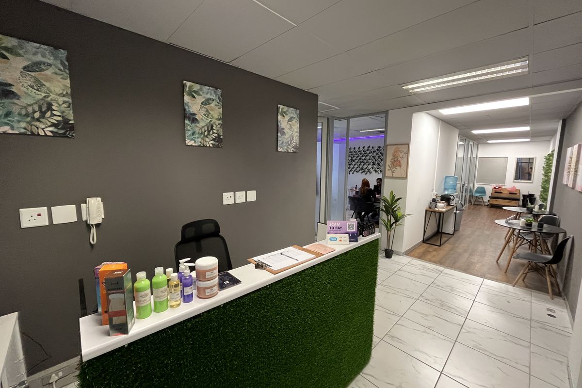 Professional office reception area featuring a modern desk, glass partitions, and a combination of tiled and laminate flooring with recessed lighting.