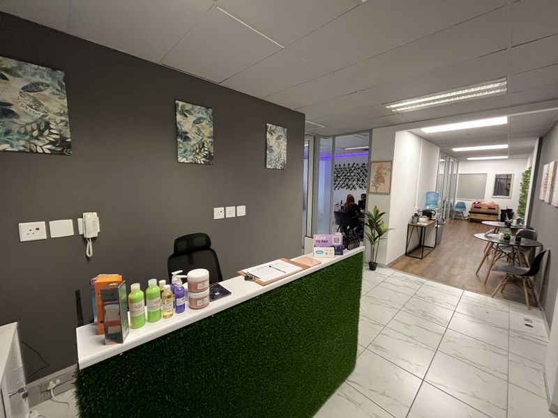 Professional office reception area featuring a modern desk, glass partitions, and a combination of tiled and laminate flooring with recessed lighting.