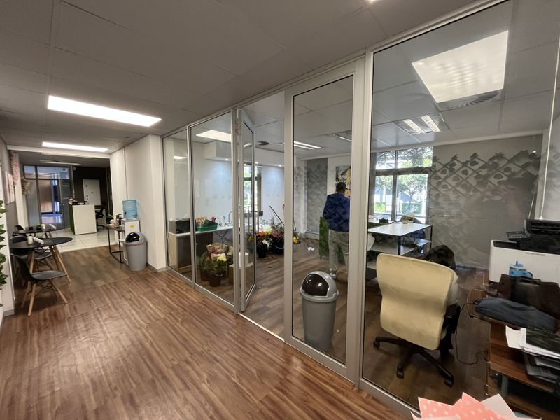 Modern office space featuring glass partition walls, suspended ceilings with recessed lighting, and durable wood-look vinyl flooring throughout the workspace.