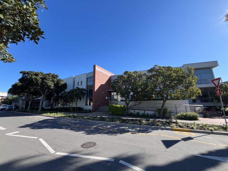 Street-level view of Hyde Park House, featuring a modern office building facade with brick accents, large glass windows, and well-maintained landscaping.