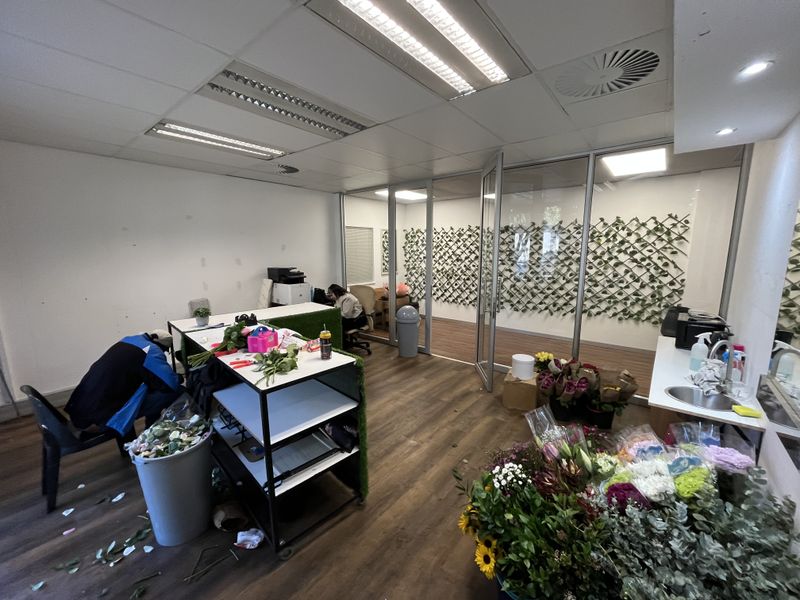 An office space featuring glass partitions, laminate flooring, and a built-in sink area, currently utilized as a floral workspace.