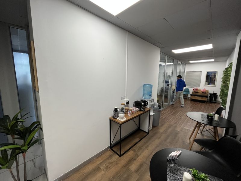 A modern office space featuring glass partitions, suspended ceilings with recessed lighting, and durable laminate flooring, creating a bright and professional work environment.
